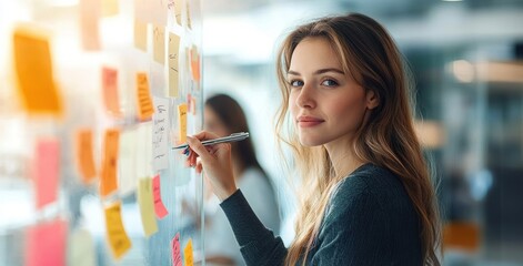 Woman focused writing on colorful sticky notes on a glass wall during collaborative brainstorming in a modern office, engaged and thoughtful