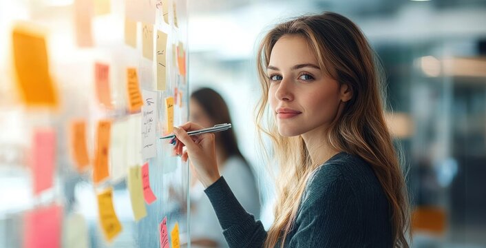 Woman focused writing on colorful sticky notes on a glass wall during collaborative brainstorming in a modern office, engaged and thoughtful
