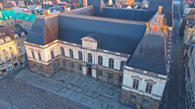 The drone rises and pulls back from the Parlement de Bretagne, revealing the empty square, quiet streets and soft sunrise light over Rennes