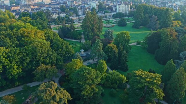 Drone shot moving forward over Parc du Thabor in Rennes, showing paths, gardens, a fountain, and the city illuminated by sunrise light.
