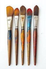 Fototapeta premium Five well used flat paintbrushes with colorful stained wooden handles and metal ferrules arranged side by side on a white background, evoking creative tactile energy