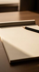 Blank lined paper notepad rests upon a polished wooden surface with a writing implement nearby.