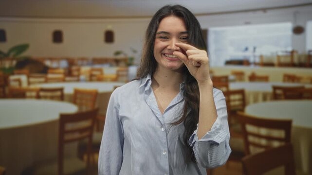 Young hispanic woman pinches fingers showing small size in restaurant building; subtle attention to detail.