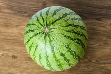 Whole ripe watermelon on a rustic wooden table, photographed from above. Fresh summer fruit with vibrant green rind and natural striped pattern.