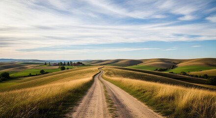 Fototapeta premium A dirt road winds through rolling hills under a partly cloudy sky.