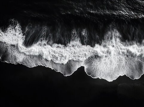 Aerial black and white view of crashing ocean waves and foamy shoreline, a dramatic moody high-contrast seascape of motion and power