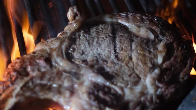 Meat cooked on grill with fire flame. Meat beef steak on grill close-up. Barbecue grill. Raw beef steak grilling. Barbecued meat and fire. Barbecued beef on smoking and flaming grill. Bbq culinary.
