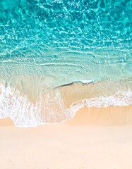 Aerial view of crystal clear turquoise ocean waves lapping onto a light beige sandy beach shoreline