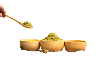 Wooden bowls with golden liquid, green powder, and spoon held by hand. Black background