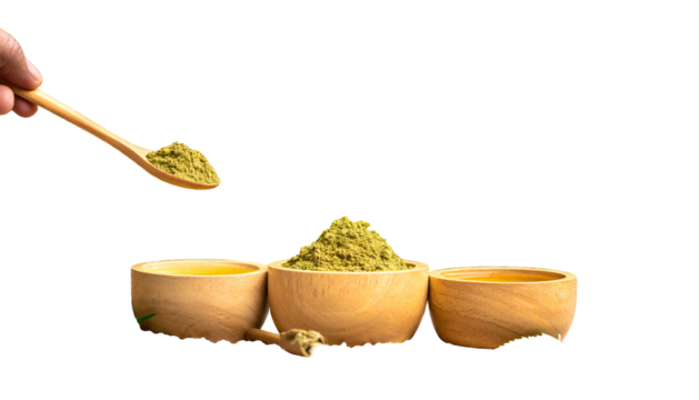 Wooden bowls with golden liquid, green powder, and spoon held by hand. Black background