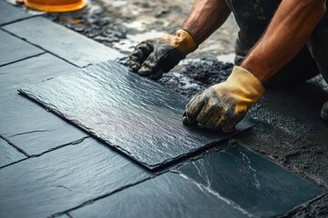 gloved worker hands carefully laying dark slate tiles on wet mortar, focused precise craftsmanship
