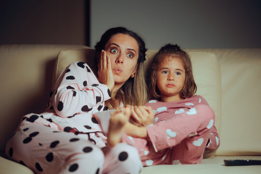 Mother and Daughter Watching TV Eating Popcorn. Family sees something shocking in cartoon show for kids 
