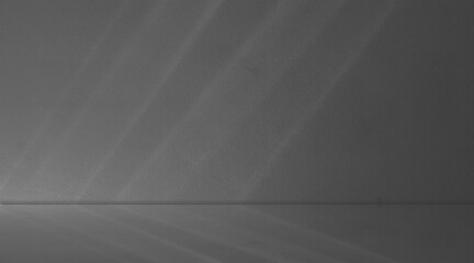Dark gray monochromatic corner empty room concrete. Diagonal bands of bright, natural light fall across surfaces from upper left, creating striking parallel highlights and shadow © sutthichai