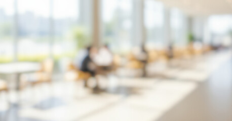 Blurred interior space with tables, chairs, and people near windows, creating a lively inviting ambience with soft glowing highlights and smooth visual depth across the scene.