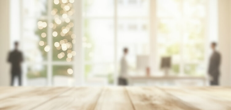 Blurry office interior with wooden foreground and silhouetted people, creating a warm professional ambience with soft glowing highlights and smooth visual depth throughout the workspace.