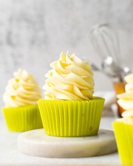 close up view of cupcakes in green liners with tall buttercream swirl, green cupcakes with vanilla buttercream with a marble background