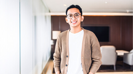 happy young Asian man in glasses standing in a modern office. Confident creative professional or startup employee looking at camera with a smile.
