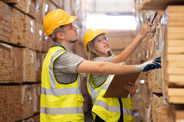 Team engineer carpenter wearing safety uniform and hard hat working holding clipboard checking quality of wooden products at workshop manufacturing. man and woman worker wood warehouse industry.