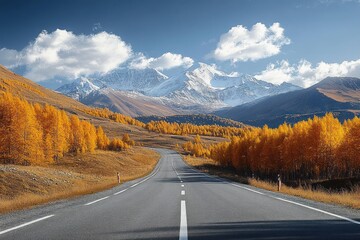 Empty highway winding through golden autumn trees toward distant snow-capped mountains under a bright blue sky, evoking calm and freedom