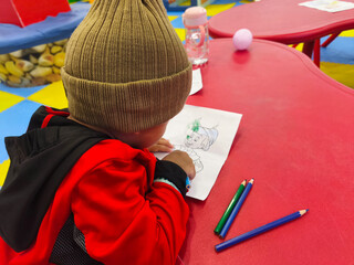 Young Child Wearing Beanie Coloring a Picture at a Kids Zone Table