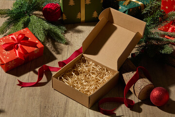 A simple tabletop scene with an open kraft box, red presents, and holiday branches. The soft...