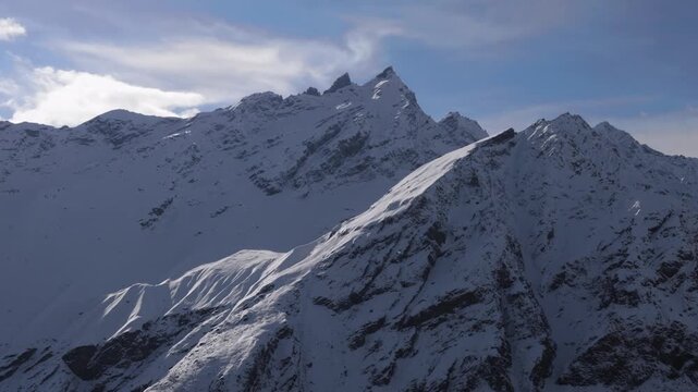 A view of the snow covered mountain range in the North Caucasus region of Russia. The footage captures the rugged, majestic peaks and vast, pristine landscapes under a partly cloudy sky, evoking a sen