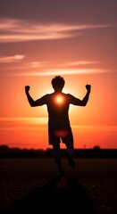 Fototapeta premium Silhouette of a soccer player celebrating with arms raised against a vibrant sunset sky