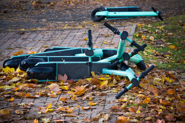 Electric scooters abandoned on a sidewalk covered in autumn leaves