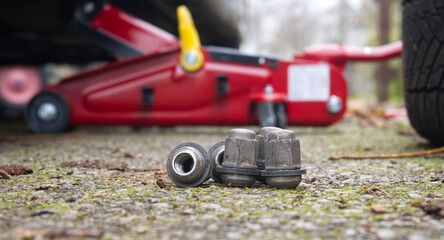 Car Jack And Wheel Nuts On Ground With Red Hydraulic Jack In Background