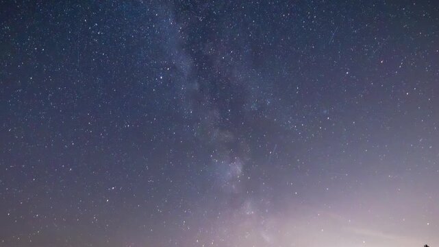milky way arcing across starry sky over treeline, silhouetted trees on horizon, faint light pollution glow,