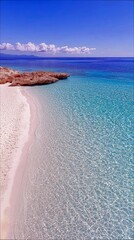 A serene tropical beach scene featuring clear turquoise water, white sand, and rocky formations under a bright blue sky.