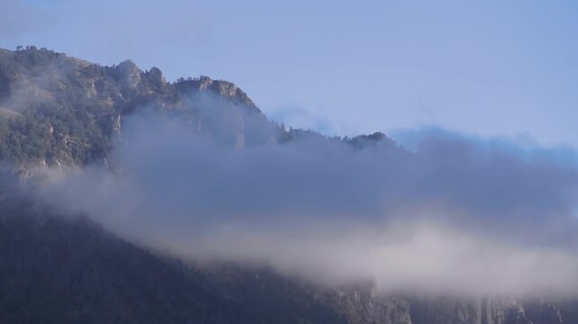 A scenic landscape view of the majestic North Caucasus mountain range in Russia, with peaks partially obscured by soft, swirling clouds.