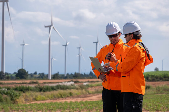 Two workers in bright orange jackets discussing project details with wind turbines in the background on a sunny day