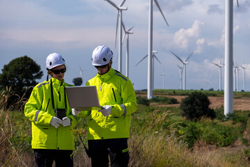 Technicians inspect wind turbines while using a laptop in a renewable energy field