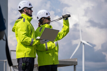 Technicians inspect wind turbine site wearing safety gear and monitoring equipment in bright green...