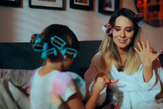 Funny Daughter Gives Her Mother a Manicure During Playtime. Little kid painting the nails of her mom having  fun
 - Powered by Adobe