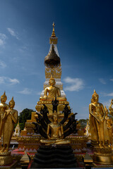 Fototapeta premium Phra That Phanom stupa with golden Buddha statues and vibrant naga serpents, showcasing ornate Thai architecture, sacred temple art, and spiritual heritage under a bright blue sky