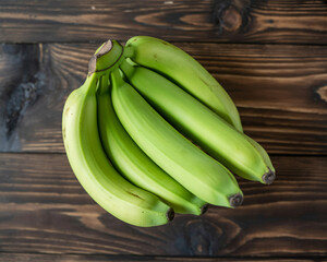 A bunch of unripe green bananas resting on a rustic dark wooden table surface, viewed from directly above.