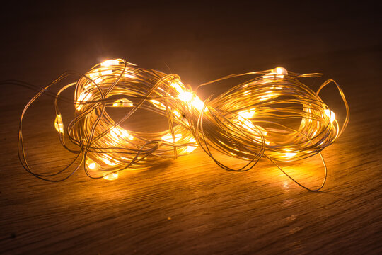Cluster of tangled fairy lights illuminates a wooden surface with a soft, warm yellow glow, creating a cozy and magical atmosphere in the dark.