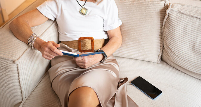 Close up of senior woman sitting on a sofa reading an ebook, representing modern senior living with copy space