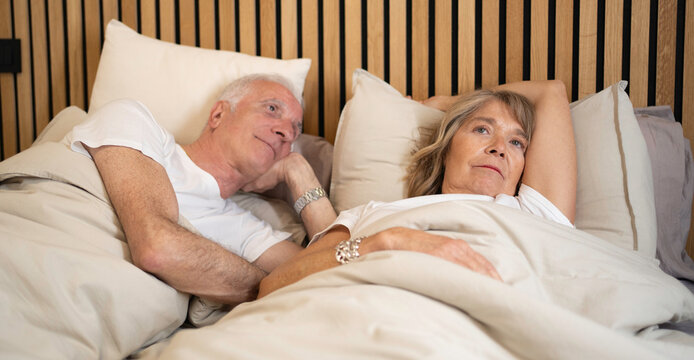 Older couple lying in bed feeling worried and thoughtful about their issues