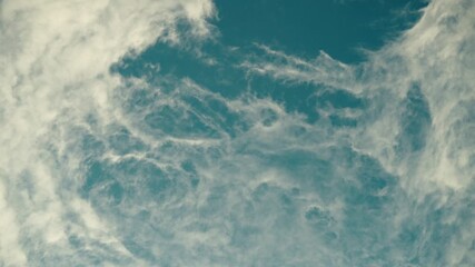 Delicate swirling clouds stretch across a bright blue sky under calm daylight