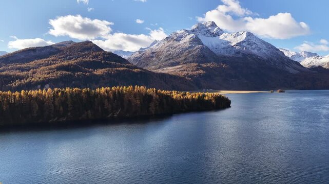 Aerial footage of Lake Sils surrounded by autumn forests and snowy alpine peaks in the Engadin valley, Switzerland.