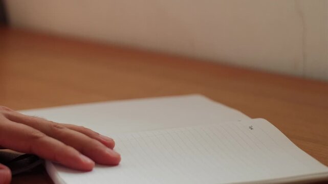 Static close-up shot of hand flipping through journal notebook pages and closing it at quiet workspace.