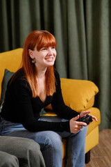 Happy woman enthusiastically plays video games on comfortable sofa in cozy living room. Gamer enjoys cozy evening with controllers in hand, unwinding after long work on weekend. Lifestyle concept.