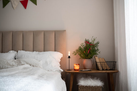 Christmas decor in interior. Fir branches in vase, candle, books in basket on wooden bench in bedroom. - Powered by Adobe