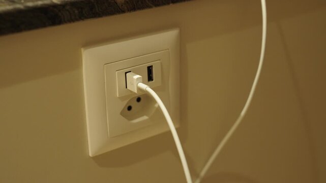 A person plugs a USB cable into a modern built-in wall socket in the kitchen &mdash; showing convenience, smart home design, and everyday practicality.