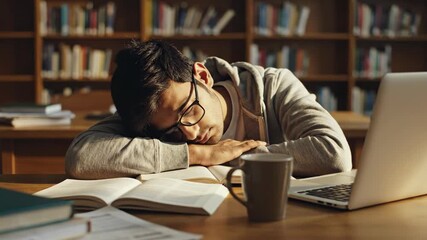A tired male student sleeping at a desk in the library. Exhausted young man napping on books after studying for an exam. Student burnout and education pressure concept - Powered by Adobe