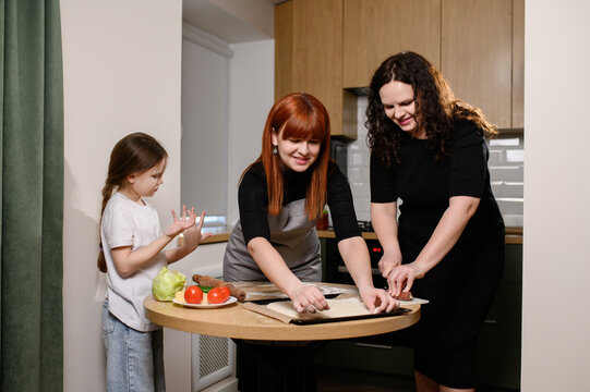Women and daughter happily cook together in kitchen. Friends cooking together, happy women create homemade pizza from fresh ingredients. Cooking masterclass, family dinner, leisure time - Powered by Adobe