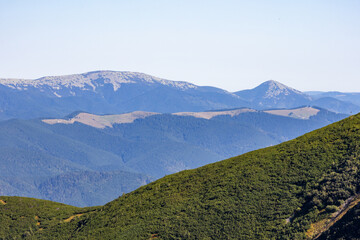 Layered blue mountain ranges fade into the distance beneath a pale sky, with a rounded green ridge in the foreground, conveying depth, scale, and serenity across a vast, wild wilderness panorama